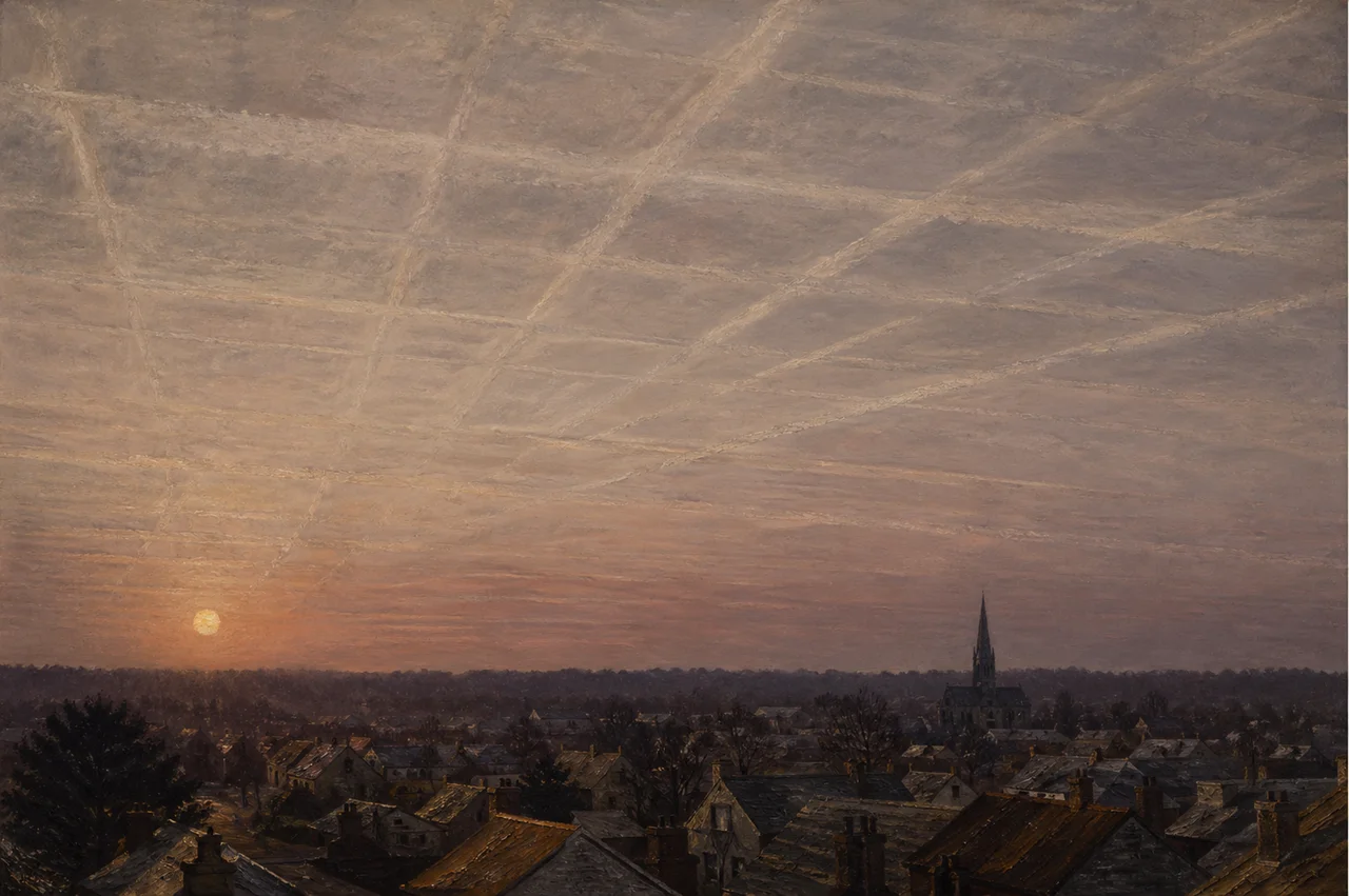 Heavy parallel white contrails crosshatching a pale late-afternoon sky above a small city, the lines lingering and widening into a uniform haze